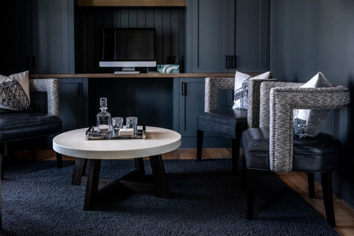 Moody dark blue mid-century conversation space with Vogel arm chairs and a round coffee table with drinks on it